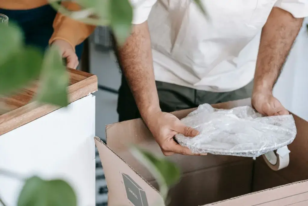 Mains déposant avec précaution une assiette emballée de papier dans une caisse