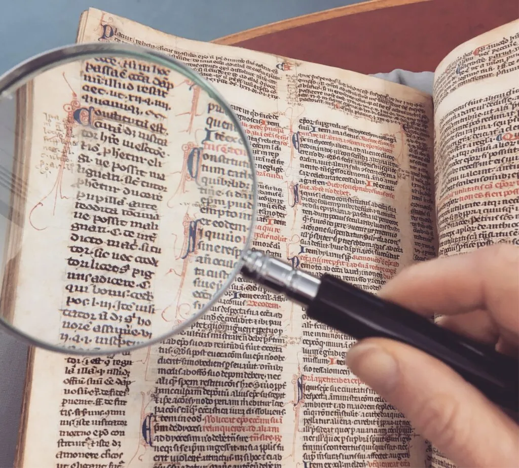 Main tenant une loupe sur la page d'un livre ancien, texte et ornements révélés en détail